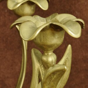 K&ouml;nnte beinhalten: Ein Messing-Kandelaber mit mehreren blumenf&ouml;rmigen Kerzenhaltern. Jeder Halter ist mit geschwungenen Bl&uuml;tenbl&auml;ttern und Stielen gestaltet, die nat&uuml;rlichen Blumen nachempfunden sind. Das Metall hat ein mattes, goldfarbenes Finish.