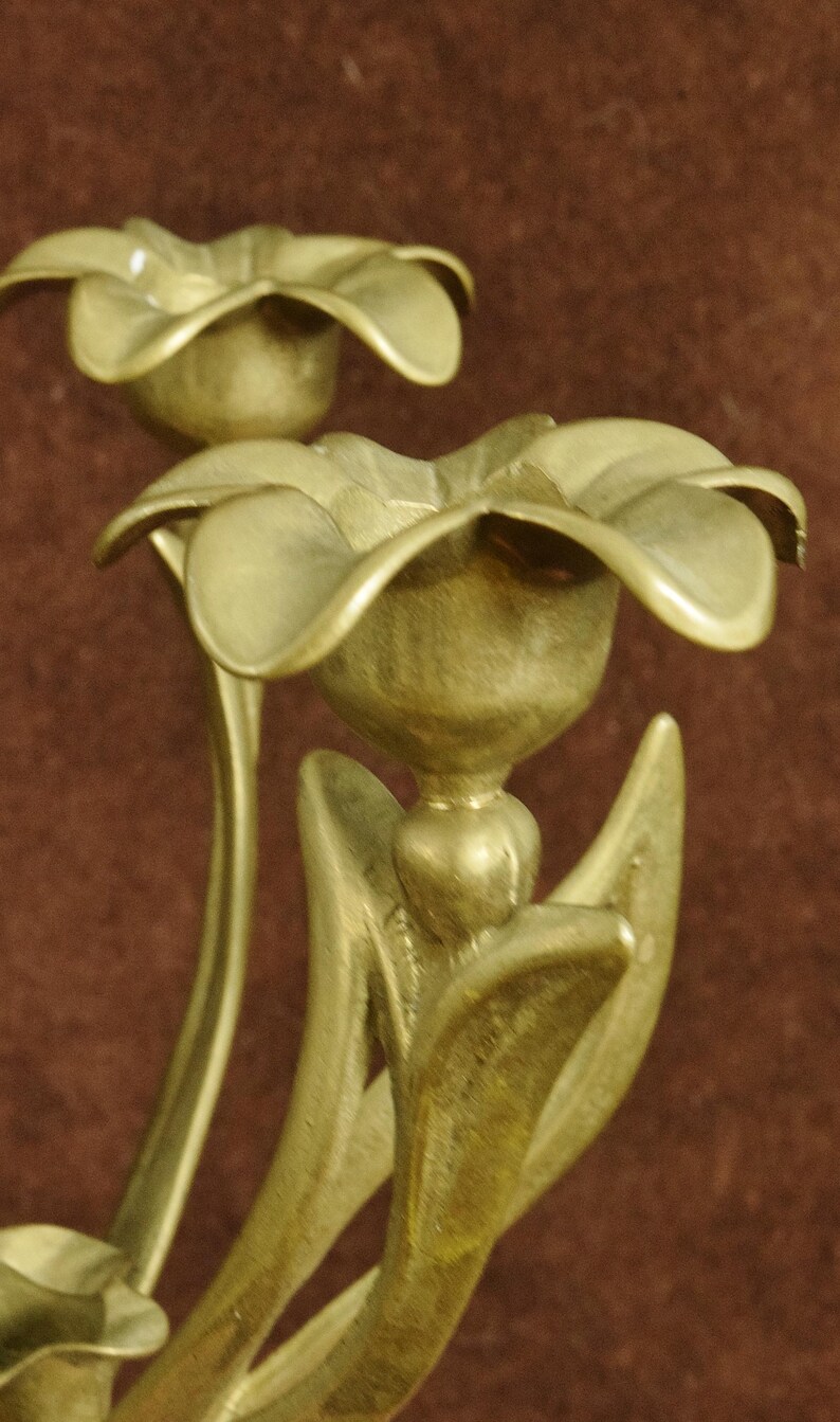 K&ouml;nnte beinhalten: Ein Messing-Kandelaber mit mehreren blumenf&ouml;rmigen Kerzenhaltern. Jeder Halter ist mit geschwungenen Bl&uuml;tenbl&auml;ttern und Stielen gestaltet, die nat&uuml;rlichen Blumen nachempfunden sind. Das Metall hat ein mattes, goldfarbenes Finish.
