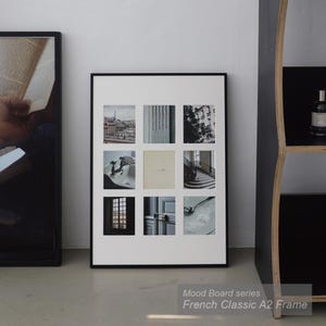 May include: A rectangular wall art piece featuring a white frame and a white mat board with nine square cutouts. Each cutout displays a different black and white or neutral-toned photograph, including architectural details, a sink, and a spoon.