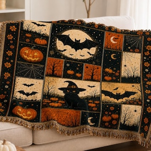 May include: A woven throw blanket featuring a Halloween-themed patchwork design with black cats wearing witch hats, flying bats, orange pumpkins, spider webs, and crescent moons in a colour palette of black, orange, and cream with fringed edges.