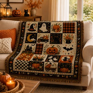 May include: A woven throw blanket featuring a grid of Halloween-themed illustrations including pumpkins, a ghost, a witch hat, a black cat, a haunted house, a bat, and a truck. The design incorporates orange, black, and cream colours with fringe.
