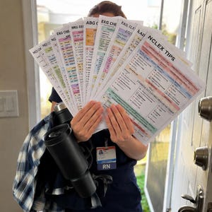 May include: A collection of nursing study guide sheets fanned out, featuring headers like NCLEX TIPS, EKG, and ABG. The papers are held alongside a black insulated tumbler and a blue and white plaid shirt, with a visible RN identification badge.