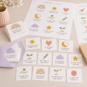 May include: A set of square cards featuring pastel illustrations of rainbows, suns, hearts, moons, clouds, stars, pencils, and sprouts. Each card includes German text such as Du lernst auf deine Weise, Schritt f&uuml;r Schritt schaffst du das, and Du bist genau richtig. The cards are displayed on a sheet and in a light purple envelope.