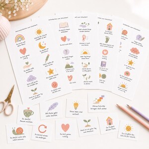 May include: A collection of white cards featuring pastel-colored illustrations and German text, including motifs like suns, hearts, snails, and rainbows. The set includes several uncut sheets and individual square cards, accompanied by scissors and two pencils.