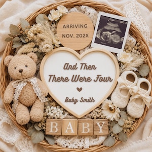 Puede incluir: Una cesta de mimbre redonda que contiene un oso de peluche color canela con una cinta de encaje, un letrero en forma de corazón con el texto And Then There Were Four Baby Smith, un disco de madera con ARRIVING NOV. 202X, una ecografía, patucos y bloques de madera con la palabra BABY.