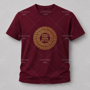 May include: A maroon short-sleeved t-shirt featuring a gold circular graphic on the chest. The design includes a Greek key border surrounding the text National African American Quilt Guild. The shirt has a crew neckline and a standard fit.