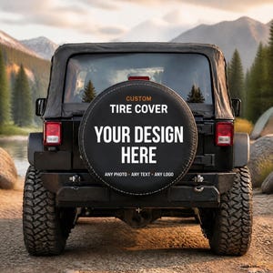 May include: A black circular spare tire cover mounted on the back of a vehicle. The cover features the text CUSTOM TIRE COVER, YOUR DESIGN HERE, and ANY PHOTO ANY TEXT ANY LOGO in white and orange lettering against a solid black background.