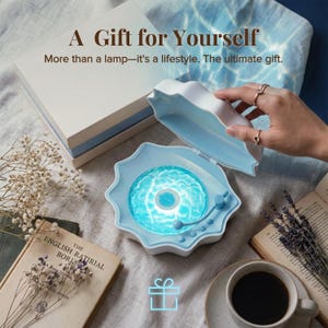 May include: A white and light blue shell-shaped lamp with a glowing blue water-effect surface and a small tonearm. The lamp features the text A Gift for Yourself and More than a lamp&mdash;it's a lifestyle. The ultimate gift. It is open and illuminated.