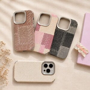 May include: Four smartphone cases with silver camera bezels. Three cases feature a patchwork fabric design with visible stitching in brown, pink and cream, and black and grey. One case is a solid cream fabric texture with a triple camera cutout.