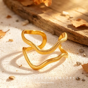 May include: A gold-toned open ring featuring two parallel, wavy bands with a textured, matte finish. The ring has an adjustable gap between the ends of the bands. The text "HANDREAMJEWELZ951" and "Handcrafted Jewellery" is visible at the bottom.