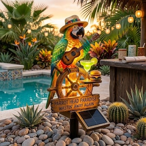 May include: A solar-powered garden statue featuring a colourful parrot wearing a straw hat, playing a ukulele, and perched on a ship's wheel. A small shelf holds a lime-garnished cocktail and a burger. A sign reads PARROT HEAD PARADISE WASTIN' AWAY AGAIN.