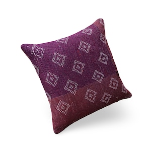 May include: A square throw pillow in deep purple and maroon tones, featuring a repeating pattern of small white stitched diamond shapes across the fabric surface. The pillow has a textured appearance with visible stitching details throughout the cover.