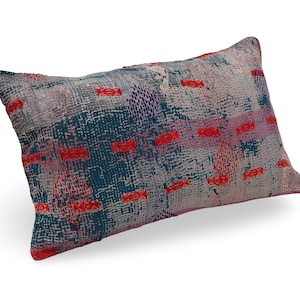 May include: A rectangular throw pillow featuring a patchwork design of layered fabrics in shades of teal, grey, and white. The surface is covered in dense, visible running stitch embroidery in bright red, purple, and dark blue thread patterns.