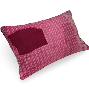 May include: A rectangular throw pillow featuring a vibrant pink fabric with a repeating white pattern. A large, solid dark maroon patch is stitched onto the left side, while the right edge displays a contrasting pink border with blue accents.