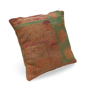 Puede incluir: Un cojín cuadrado con una superficie de tela texturizada y un diseño de patchwork en tonos naranja quemado, óxido y verde apagado. El tejido muestra patrones de costura visibles en toda la superficie y una pequeña cremallera metálica en el borde.