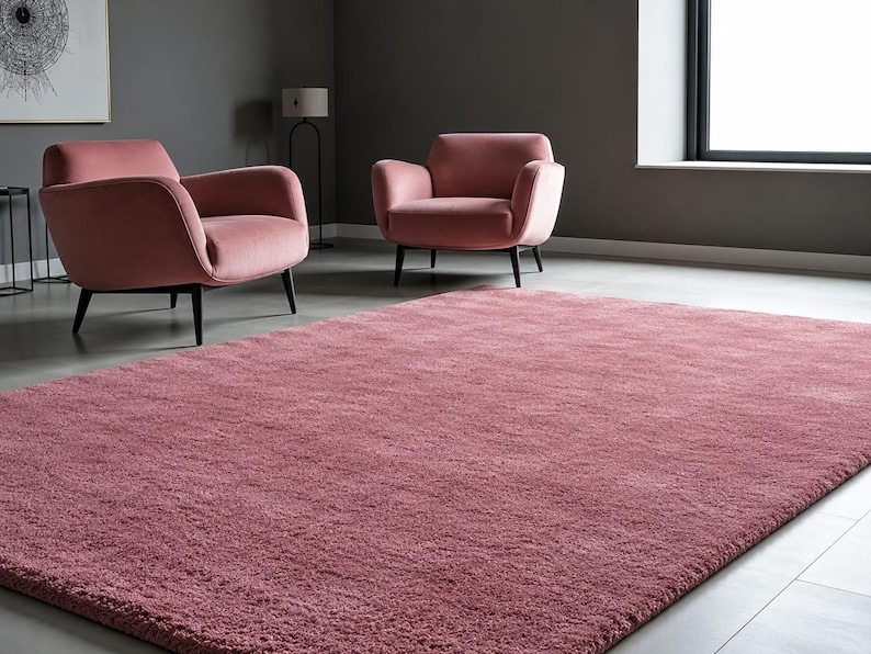 May include: A rectangular, solid dusty rose area rug with a thick, textured pile surface. The rug features a uniform, deep pink colour throughout its entire expanse, providing a soft and plush appearance that covers the floor space in the room.