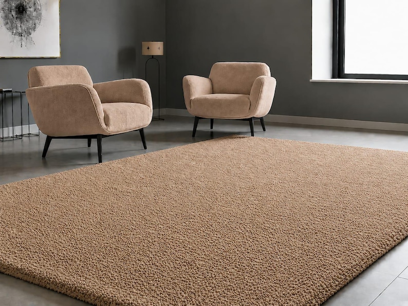 May include: A large, rectangular area rug with a thick, textured, tan-coloured pile. The rug features a dense, looped surface construction that covers the floor, providing a uniform, solid-coloured appearance across its entire visible surface area.