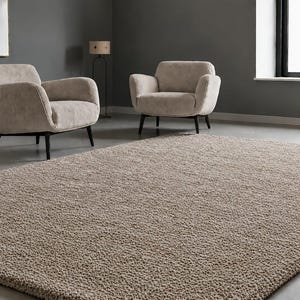 May include: A large rectangular area rug with a thick, textured, beige pile surface. The rug features a dense, looped construction and is positioned in a room with two matching beige upholstered armchairs with black wooden legs.