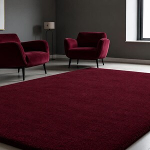 May include: A large, rectangular, deep burgundy area rug with a dense, plush texture covering the floor. The rug features a solid, uniform colour throughout its surface, providing a soft and consistent appearance across the entire floor space.