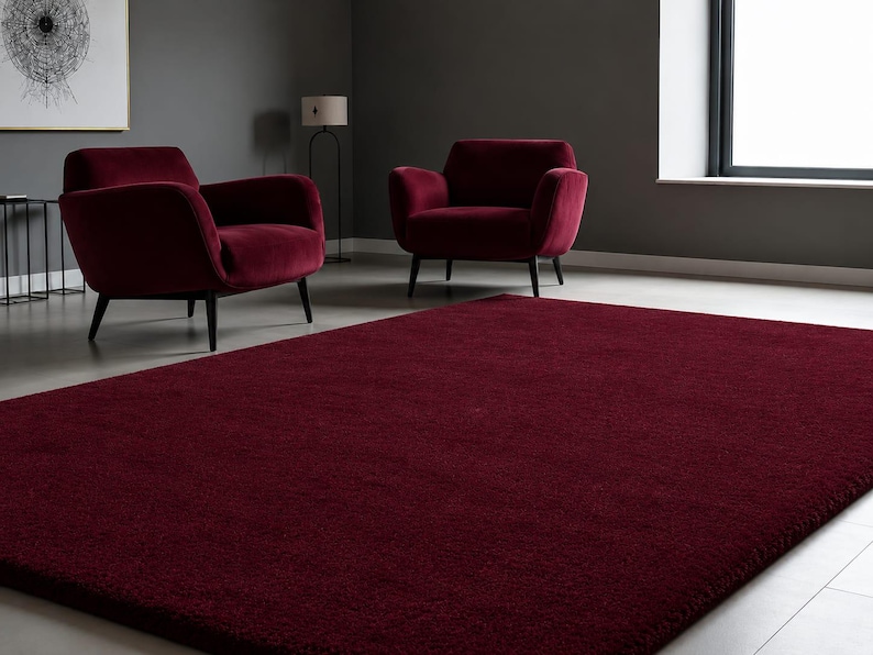 May include: A large, rectangular, deep burgundy area rug with a dense, plush texture covering the floor. The rug features a solid, uniform colour throughout its surface, providing a soft and consistent appearance across the entire floor space.