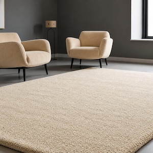 May include: A large, rectangular, cream-coloured area rug with a thick, textured, high-pile surface. The rug is positioned in the foreground, covering the floor in front of two matching cream-coloured armchairs with dark, tapered wooden legs.