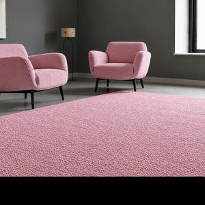 May include: A large, rectangular, textured pink area rug with a dense, looped pile surface. The rug features a uniform solid pink colour throughout its entire expanse, providing a soft and consistent visual appearance across the floor space.