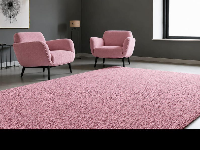 May include: A large, rectangular, textured pink area rug with a dense, looped pile surface. The rug features a uniform solid pink colour throughout its entire expanse, providing a soft and consistent visual appearance across the floor space.