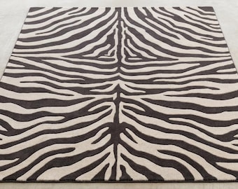 Op de afbeelding: Een rechthoekig vloerkleed met een contrastrijk zebrastrepenpatroon in donkerbruin en crème. Het ontwerp bestaat uit organische, vloeiende lijnen die vanuit een centrale as uitstralen, wat een symmetrisch visueel effect op het oppervlak creëert.