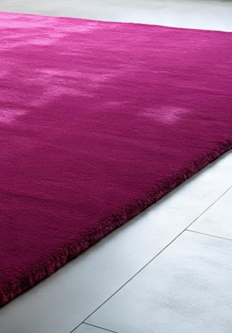 May include: A rectangular area rug in a deep magenta hue with a soft, plush, and dense pile texture. The rug features subtle variations in colour intensity across its surface, creating a soft, cloud-like visual effect throughout the fabric.