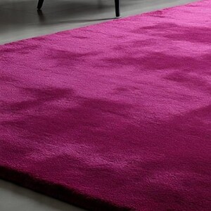 May include: A plush, deep magenta area rug with a thick, soft-textured pile. The rug features a solid, vibrant fuchsia colour that covers the entire surface, providing a dense and uniform appearance across the rectangular floor covering.