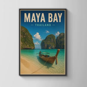 May include: A framed travel poster featuring a long-tail boat anchored in the turquoise waters of Maya Bay, Thailand. The scene includes towering limestone cliffs, a sandy beach, and a blue sky with clouds. The text reads MAYA BAY THAILAND.