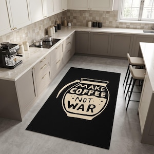 Puede incluir: Una alfombra rectangular negra con un gráfico grande de color crema que muestra una cafetera con forma de granada de mano. El diseño incluye el texto "MAKE COFFEE NOT WAR" en letras mayúsculas y negritas, centrado dentro de la ilustración.