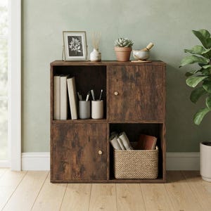 May include: A dark brown wood-grain storage cabinet with four square compartments. Two compartments feature doors with small gold knobs, while the other two are open. The unit holds books, two cylindrical pen holders, and a woven basket.