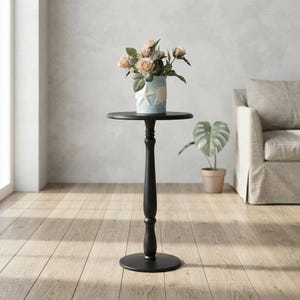 May include: A black pedestal side table with a round top and a central column base. A light blue vase with a white starfish design sits on the table, containing a bouquet of light pink roses and green leaves with visible stems and petals.