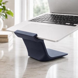 Puede incluir: Un soporte para portátil de color azul oscuro y forma curva que sostiene un ordenador plateado con teclado negro. El soporte cuenta con una base sólida e inclinada y un borde frontal que mantiene el dispositivo en una posición elevada.