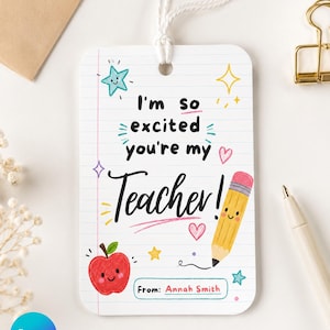 May include: A rectangular white gift tag with rounded corners and a white string, featuring lined paper graphics, a smiling red apple, a smiling yellow pencil, and colorful stars and hearts. The text reads: I'm so excited you're my Teacher! From: Annah Smith.