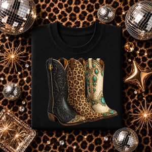 Pode incluir: Uma t-shirt preta com uma estampa gráfica de três botas de cowboy. A bota esquerda é preta com padrões florais em relevo e detalhes dourados, a bota do meio tem estampa de leopardo e a direita é de cor creme com pedras turquesas.