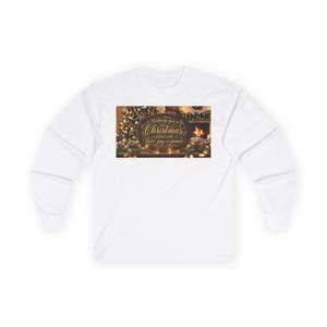 Puede incluir: Una camiseta blanca de manga larga con un estampado gráfico rectangular de un letrero ovalado oscuro con texto dorado en cursiva que dice Wishing you a Christmas filled with love, joy and peace, sobre un fondo borroso de un árbol de Navidad.