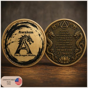 May include: Two circular bronze-toned sobriety coins. The left coin features a black dragon silhouette, the letter A, and the text Awaken The Dragon Within. The right coin displays two dragons, a triangle symbol, a lotus flower, and the text 2 Years.
