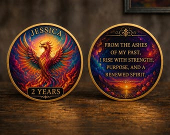 Op de afbeelding: Twee ronde medaillons met een gouden rand. Het linker medaillon toont een kleurrijke feniks, de naam JESSICA en de tekst 2 YEARS. Het rechter medaillon bevat de tekst FROM THE ASHES OF MY PAST, I RISE WITH STRENGTH, PURPOSE, AND A RENEWED SPIRIT.