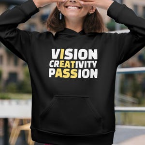 May include: A black long-sleeve hooded sweatshirt featuring the white text VISION, CREATIVITY, and PASSION printed on the front. The letter I in each word is highlighted in yellow, forming the vertical word IDEAS in yellow text.