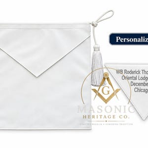 May include: A white Masonic apron featuring a triangular flap, white tassels on cords, and a gold square and compass emblem. A separate view shows a personalized flap with the text WB Roderick Thompson, KYCH, Oriental Lodge #68, PHA, December 2022, Chicago, IL.