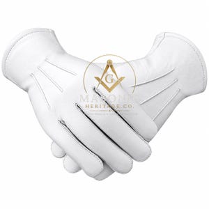 Pu&ograve; includere: Un paio di guanti in pelle bianca con tre linee di cucitura decorative sul dorso della mano. Un logo color oro con il simbolo di squadra e compasso e il testo MASONIC HERITAGE CO. &egrave; centrato sopra i guanti.