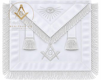 Può includere: Un grembiule cerimoniale bianco con una patta triangolare e un simbolo dell'occhio ricamato al centro. Il grembiule include due nappe bianche, un emblema di squadra e compasso con la lettera G e una frangia bianca decorativa sui bordi.