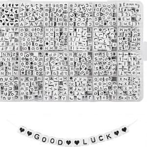 May include: A rectangular clear plastic storage container divided into twenty-eight compartments filled with white cube-shaped beads featuring black letters and heart symbols. Below the container is a string of beads spelling out GOOD LUCK.