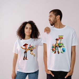 May include: Two white short-sleeved t-shirts featuring Toy Story 5 graphic prints. One shirt displays Woody and Buzz Lightyear, while the other features a group of characters including Woody, Buzz Lightyear, Mr. Potato Head, and Ducky with the Toy Story 5 logo.