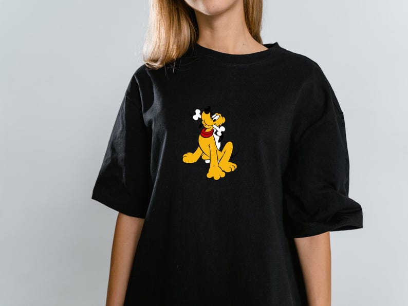 Może przedstawiać: Czarny t-shirt z kr&oacute;tkim rękawem z centralną grafiką przedstawiającą ż&oacute;łtego psa z kresk&oacute;wki Pluto, kt&oacute;ry ma na sobie czerwoną obrożę i trzyma w pysku białą kość. Koszulka ma okrągły dekolt oraz luźny kr&oacute;j z szerokimi rękawami.
