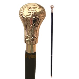 May include: A walking stick featuring a polished gold-tone metal handle with embossed floral patterns and a smooth black shaft. The handle has a rounded, bulbous shape with intricate detailing. The brand name Riylox is printed on the shaft.