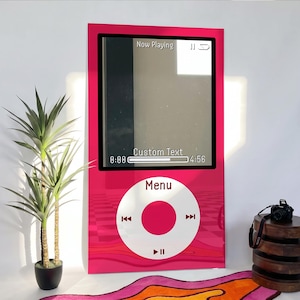 May include: A rectangular wall art piece featuring a bright pink digital music player design. The screen displays the text Now Playing, Custom Text, 0:00, and 4:56. Below the screen is a white circular control wheel with Menu and playback icons.