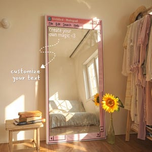 Può includere: Un alto specchio rettangolare da terra con una cornice rosa progettata per assomigliare a una finestra di blocco note del computer. La barra superiore mostra 'Untitled - Notepad' con menu. Il vetro presenta il testo bianco 'create your own magic <3'.